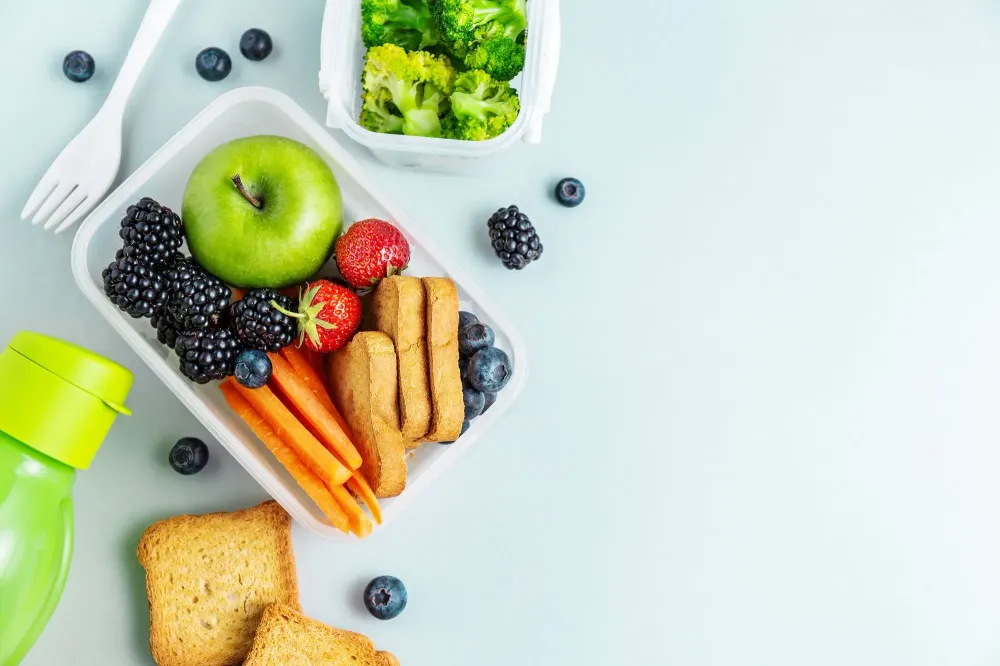 Overhead view of a packed lunch full of fruits and vegetables on a pale blue table